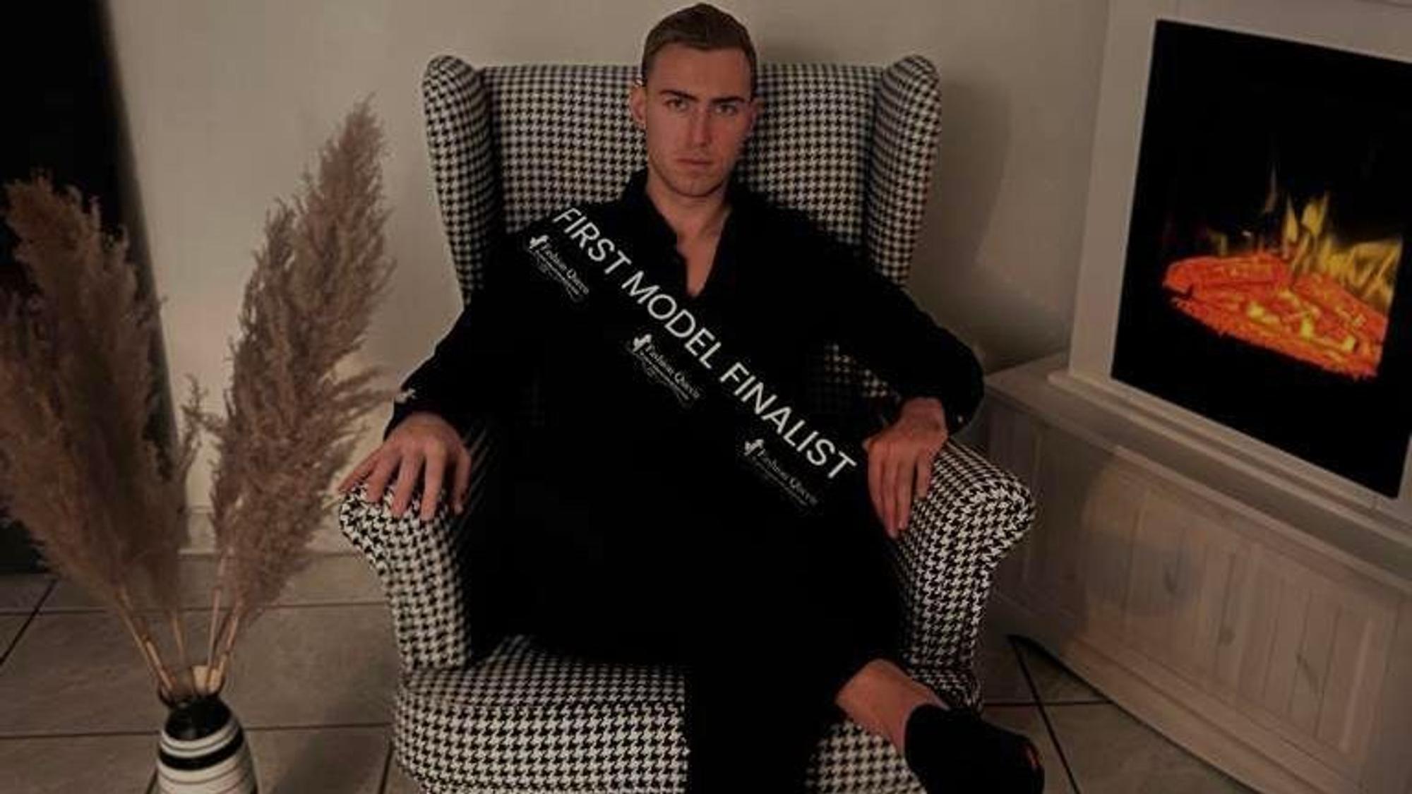 Dennis aus Erftstadt sitzt in einem Sessel, er trägt eine Schärpe mit der Aufschrift „First Model Finalist“.