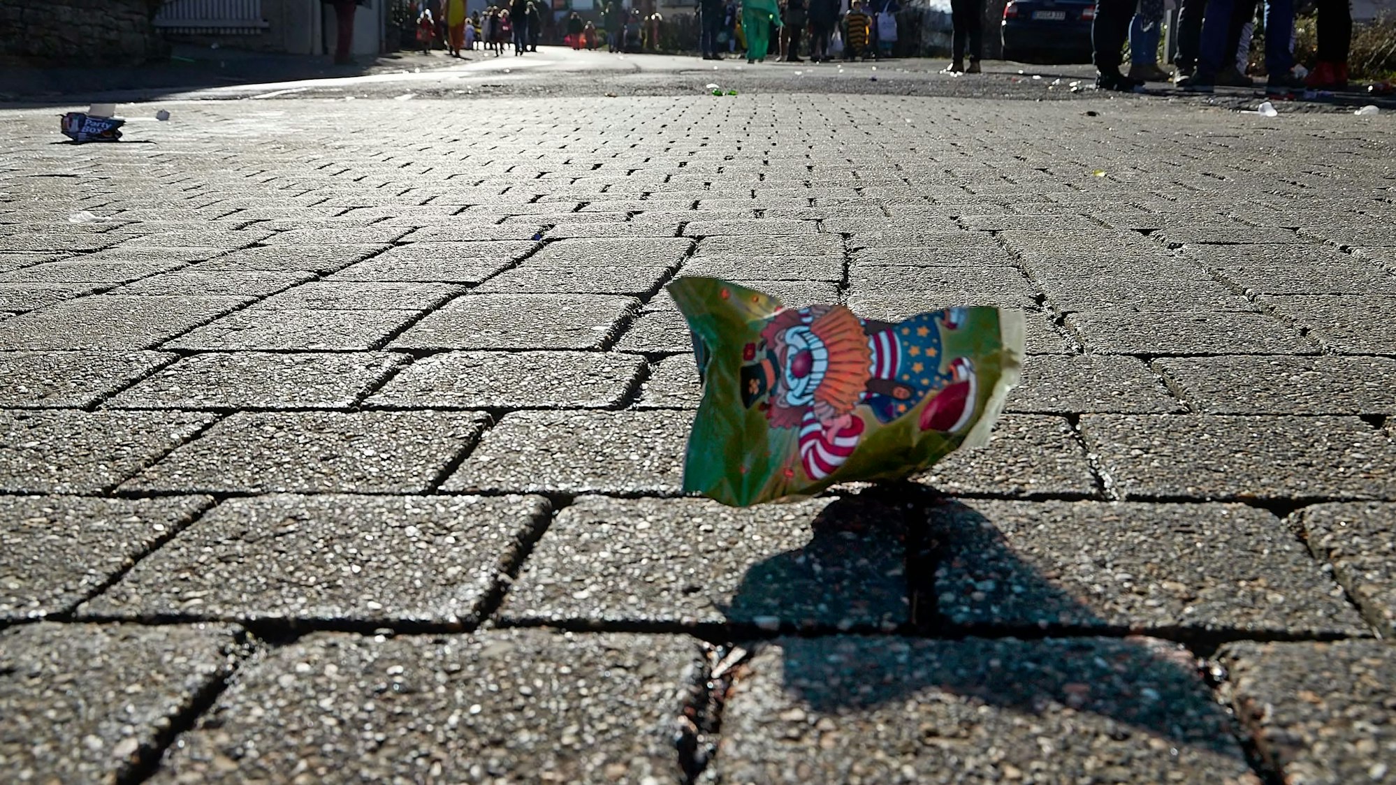 Eine Chipstüte liegt nach einem Karnevalszug auf dem Straßenpflaster.
