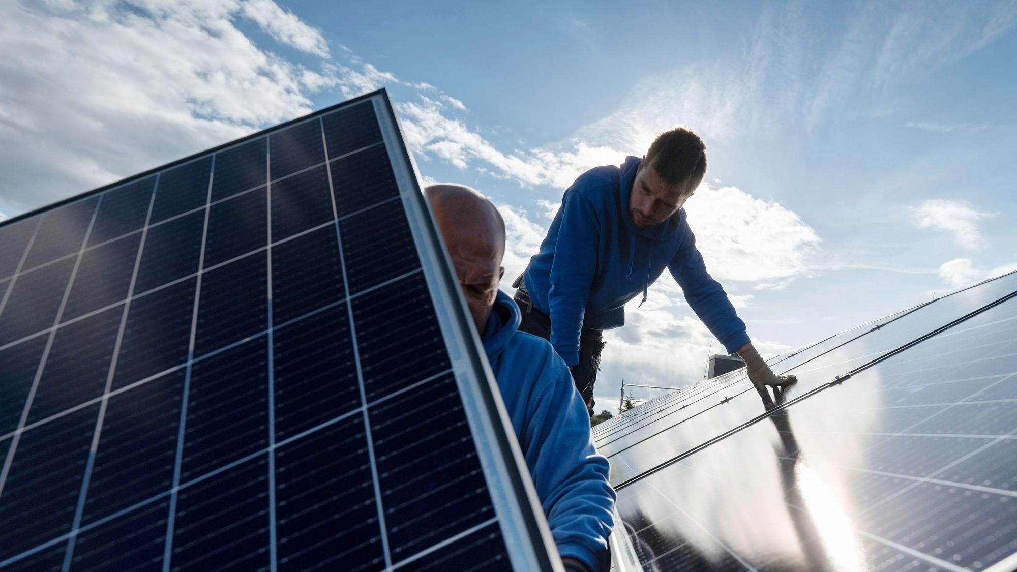 Arbeiter montieren Photovoltaikmodule auf dem Dach eines Wohnhauses.