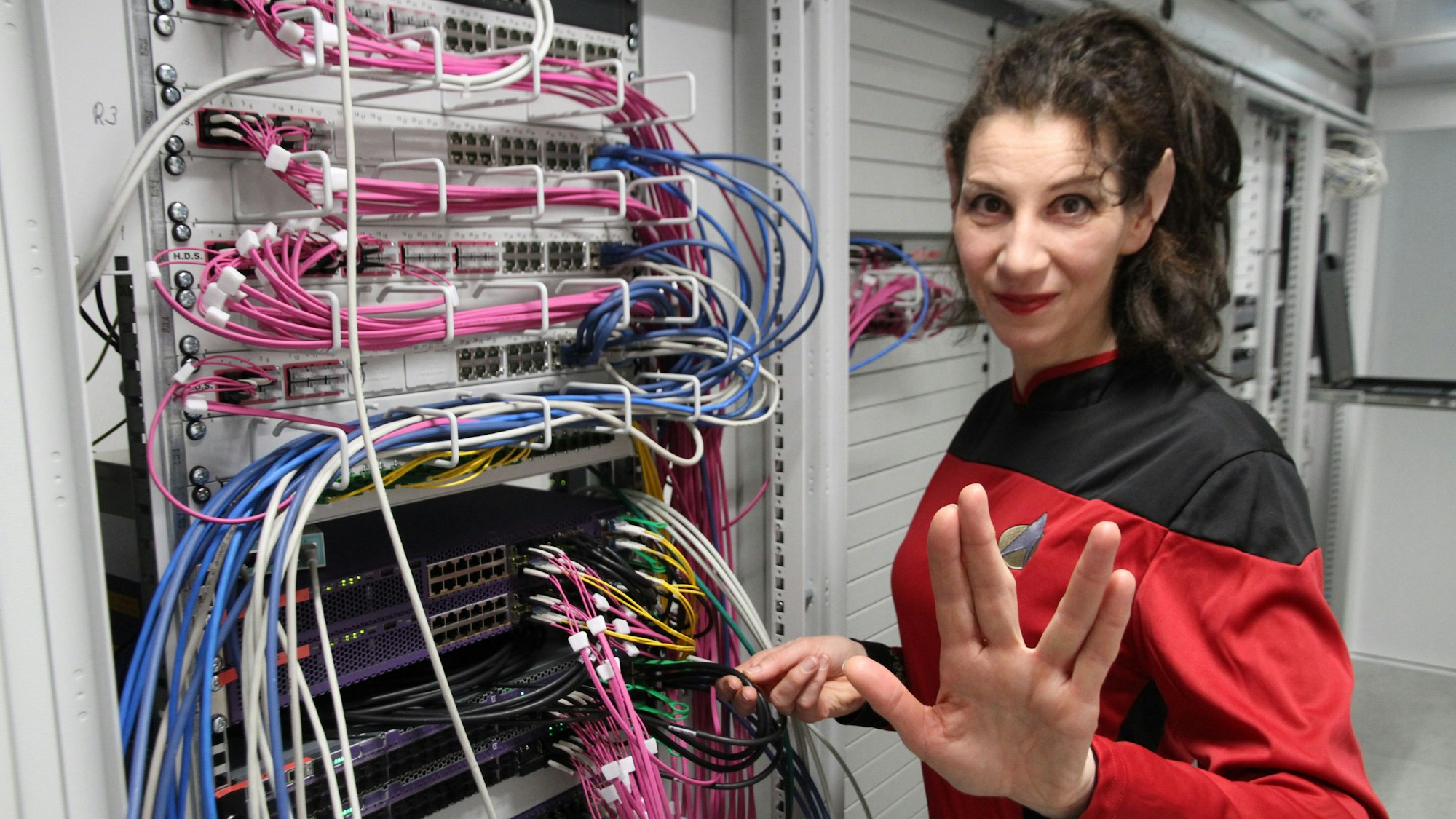 Sandra Ebert als Commander Roswitha Ipley steht neben vielen Kabeln und macht den Vulkanier-Gruß.