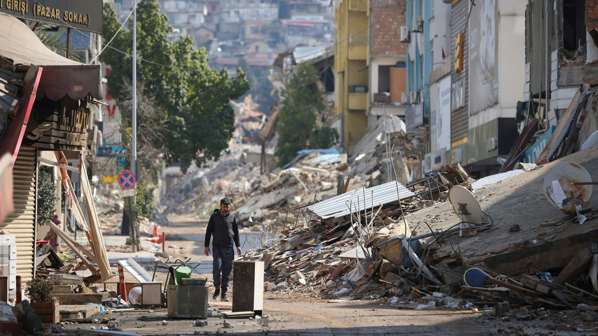 21.02.2023, Türkei, Antakya: Ein Mann geht an zerstörten Gebäuden entlang. Nach dem verheerenden Erdbeben am 06.02.2023 in der türkisch-syrischen Grenzregion kommt es immer wieder zu heftigen Nachbeben. Bei dem erneuten Erdbeben in der Südosttürkei ist die Zahl der Todesopfer weiter gestiegen. Foto: Unal Cam/AP/dpa +++ dpa-Bildfunk +++