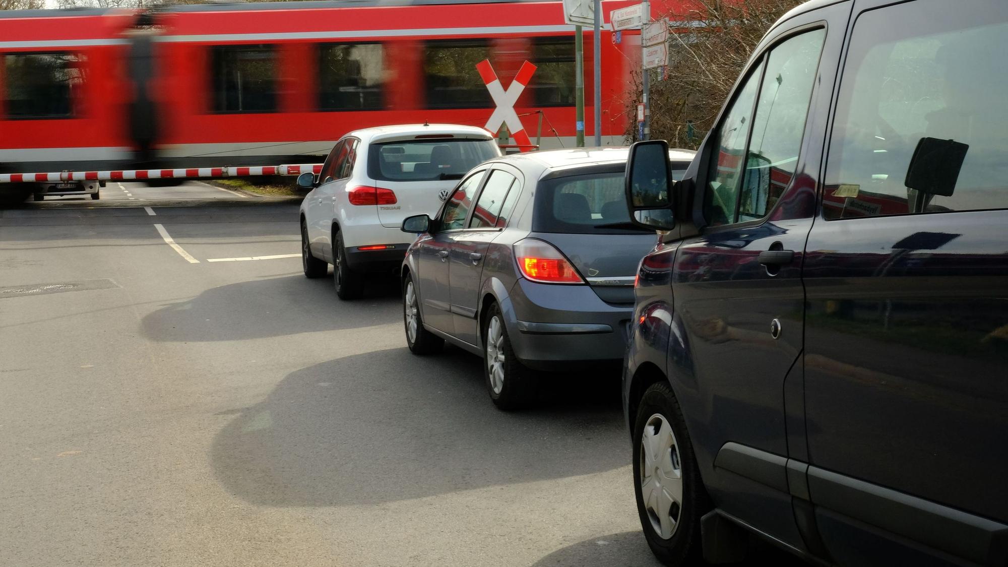 An einer geschlossenen Bahnschranke staut sich der Autoverkehr. Ein Zug fährt vorbei.