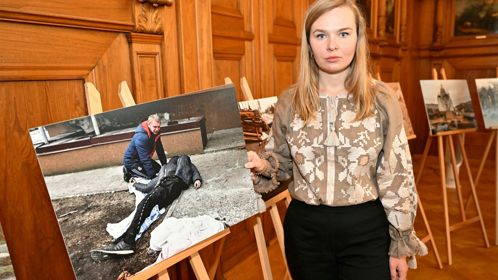 Alina Saraniuk aus Butscha steht im Bergisch Gladbacher Ratssaal mit einem Bild der Gräueltaten in ihrer Heimatstadt.
