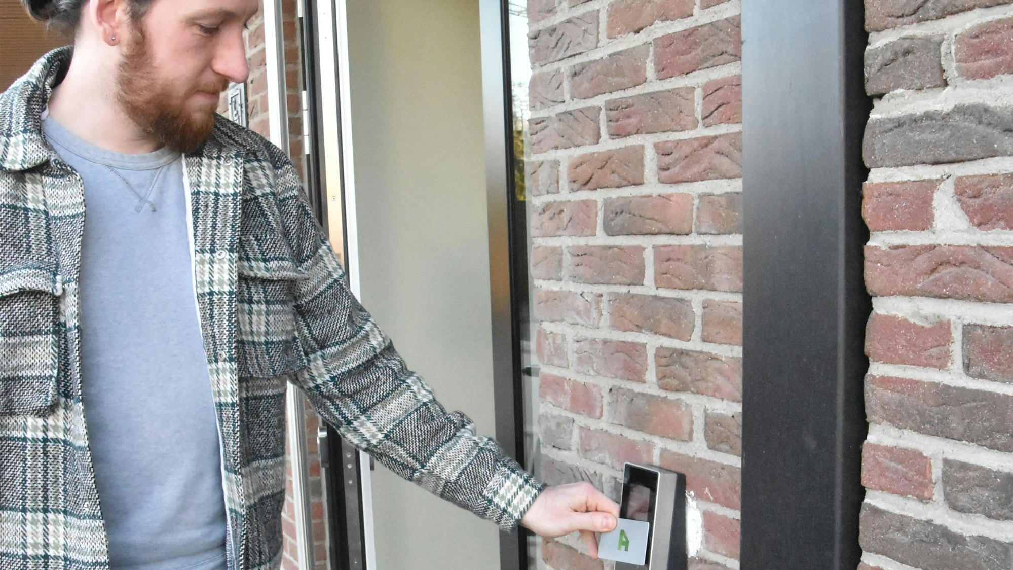 Ein Mann hält eine Chipkarte vor ein Gerät, das an einer Hauswand befestigt ist.