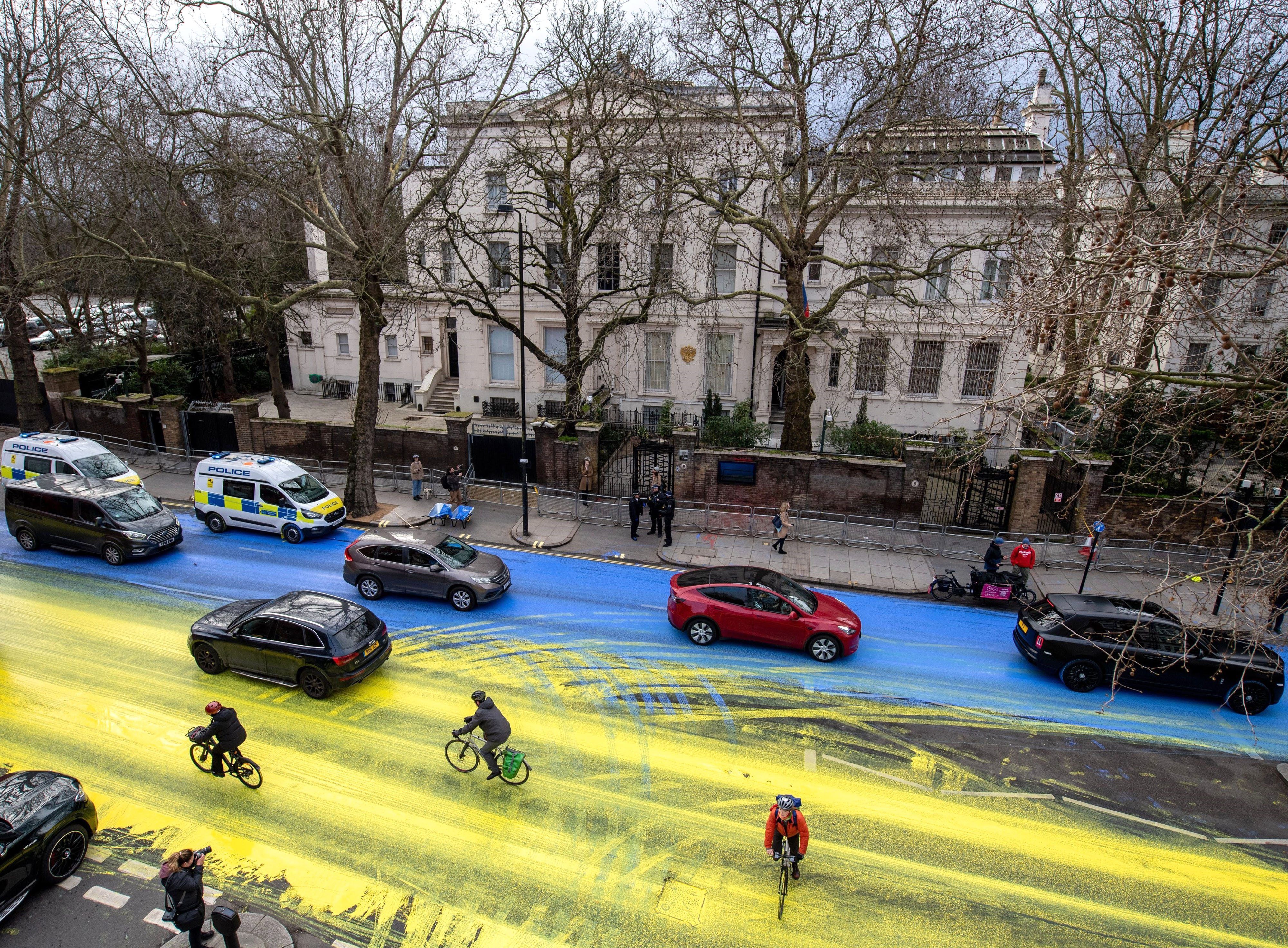 London: Fahrradfahrer fahren über eine Straße vor der russischen Botschaft, die von Demonstranten in den Farben der ukrainischen Flagge angemalt wurde.
