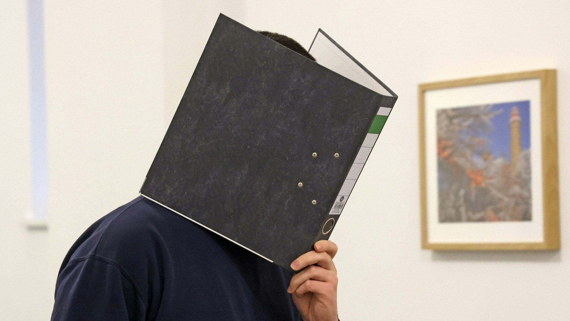 Man sieht eine Person, die sich einen Ordner vor das Gesicht hält.