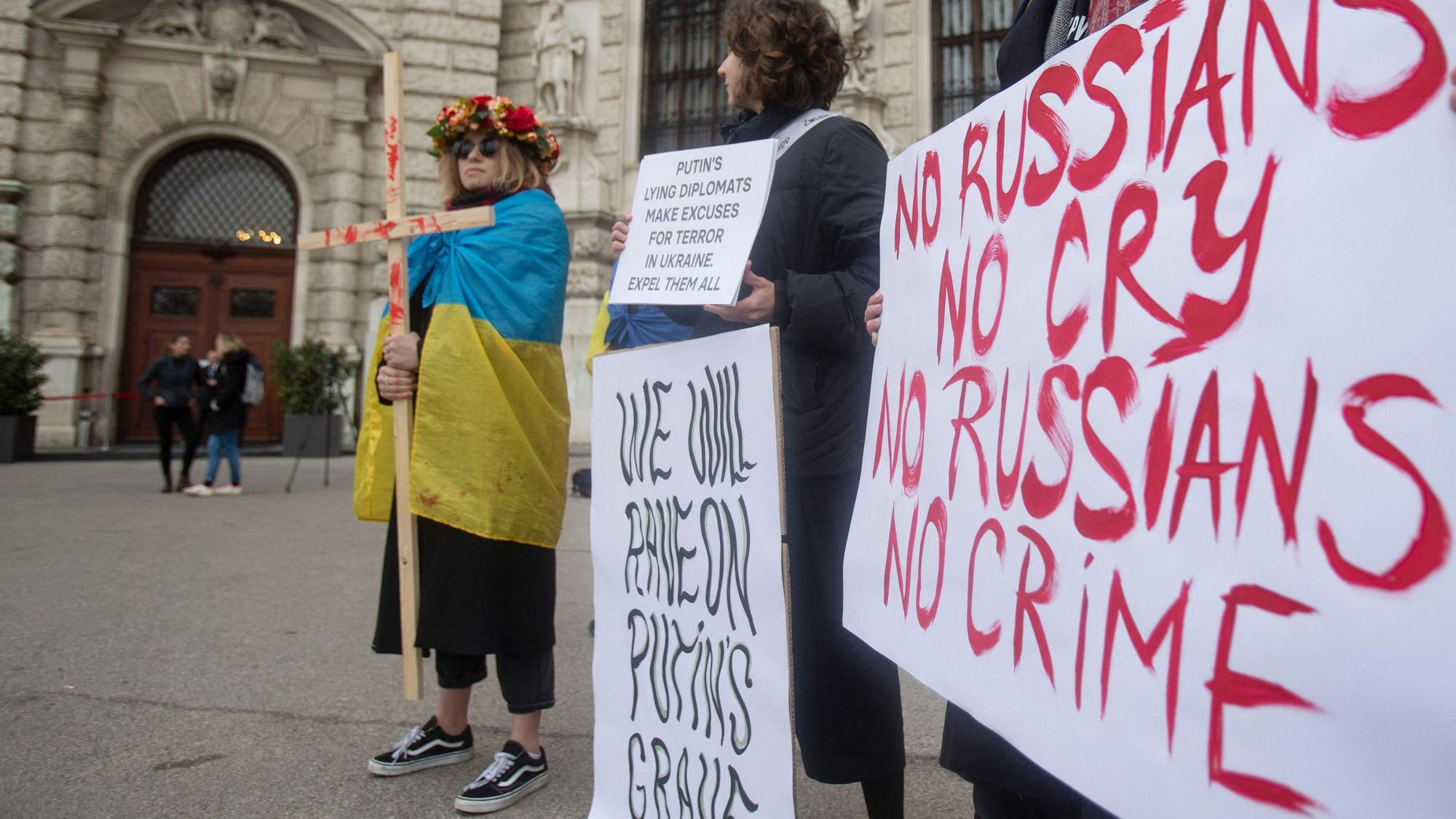 Demonstranten halten Plakate mit der Aufschrift „No Russians, no cry – no Russians no crime“ vor der Wiener Hofburg in der Hand. Eine Person trägt eine ukrainische Flagge um die Schultern und hält ein Kreuz in der Hand.