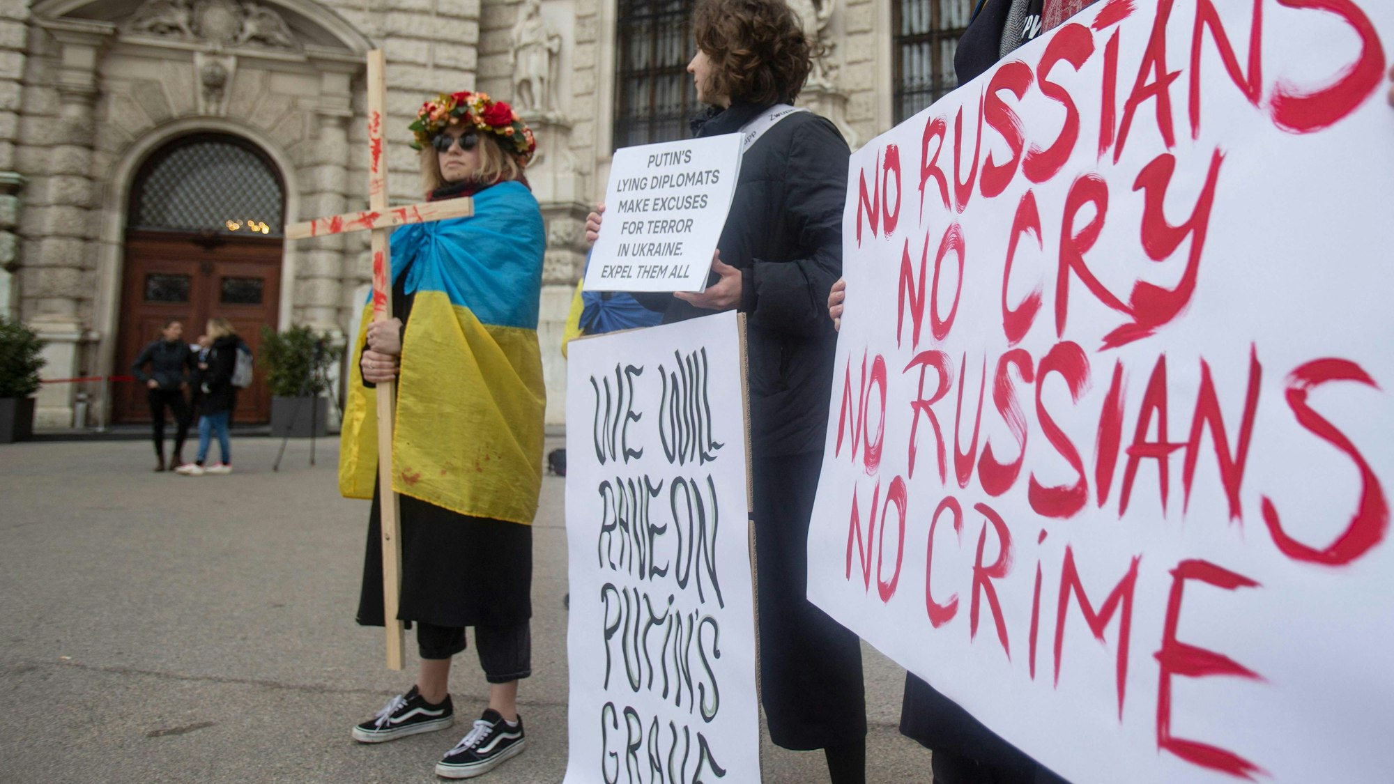 Demonstranten halten Plakate mit der Aufschrift „No Russians, no cry – no Russians no crime“ vor der Wiener Hofburg in der Hand. Eine Person trägt eine ukrainische Flagge um die Schultern und hält ein Kreuz in der Hand.