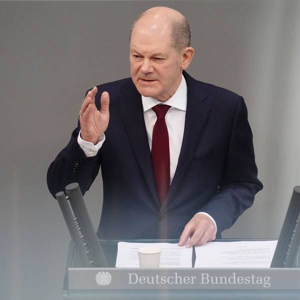 Bundeskanzler Olaf Scholz steht am Rednerpult des Bundestags. Er hat eine Hand erhoben.