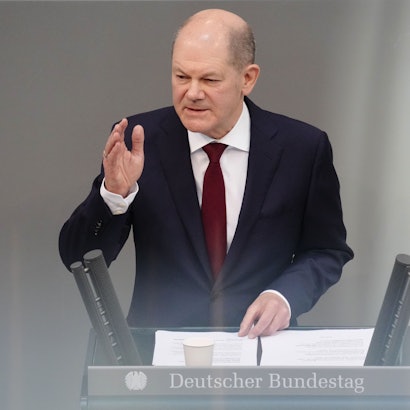 Bundeskanzler Olaf Scholz steht am Rednerpult des Bundestags. Er hat eine Hand erhoben.