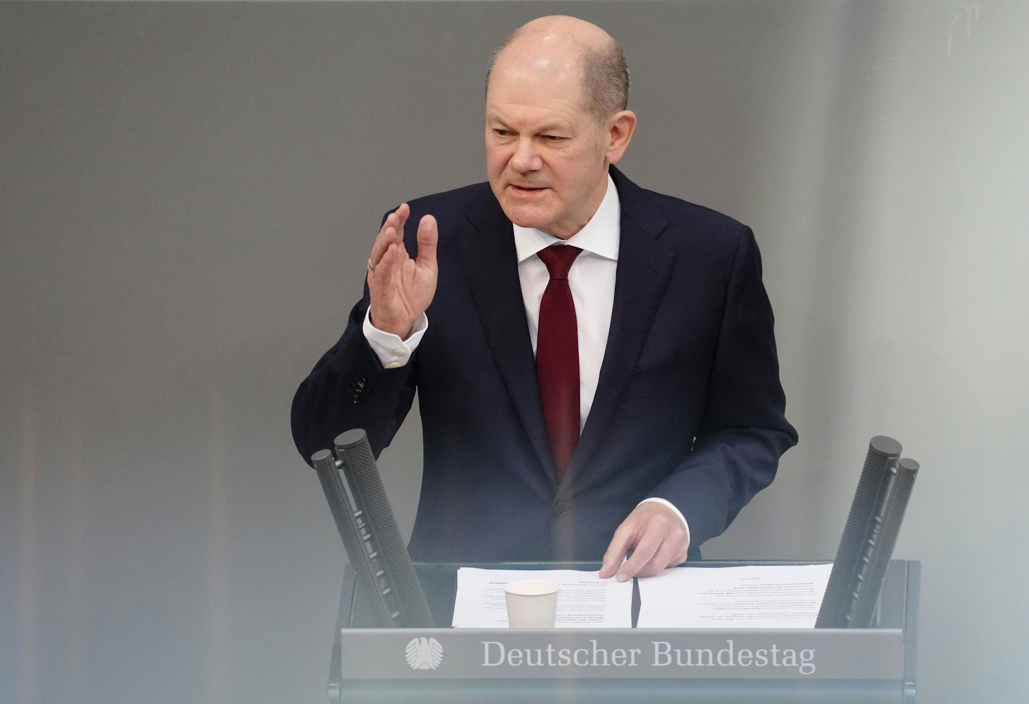 Bundeskanzler Olaf Scholz steht am Rednerpult des Bundestags. Er hat eine Hand erhoben.
