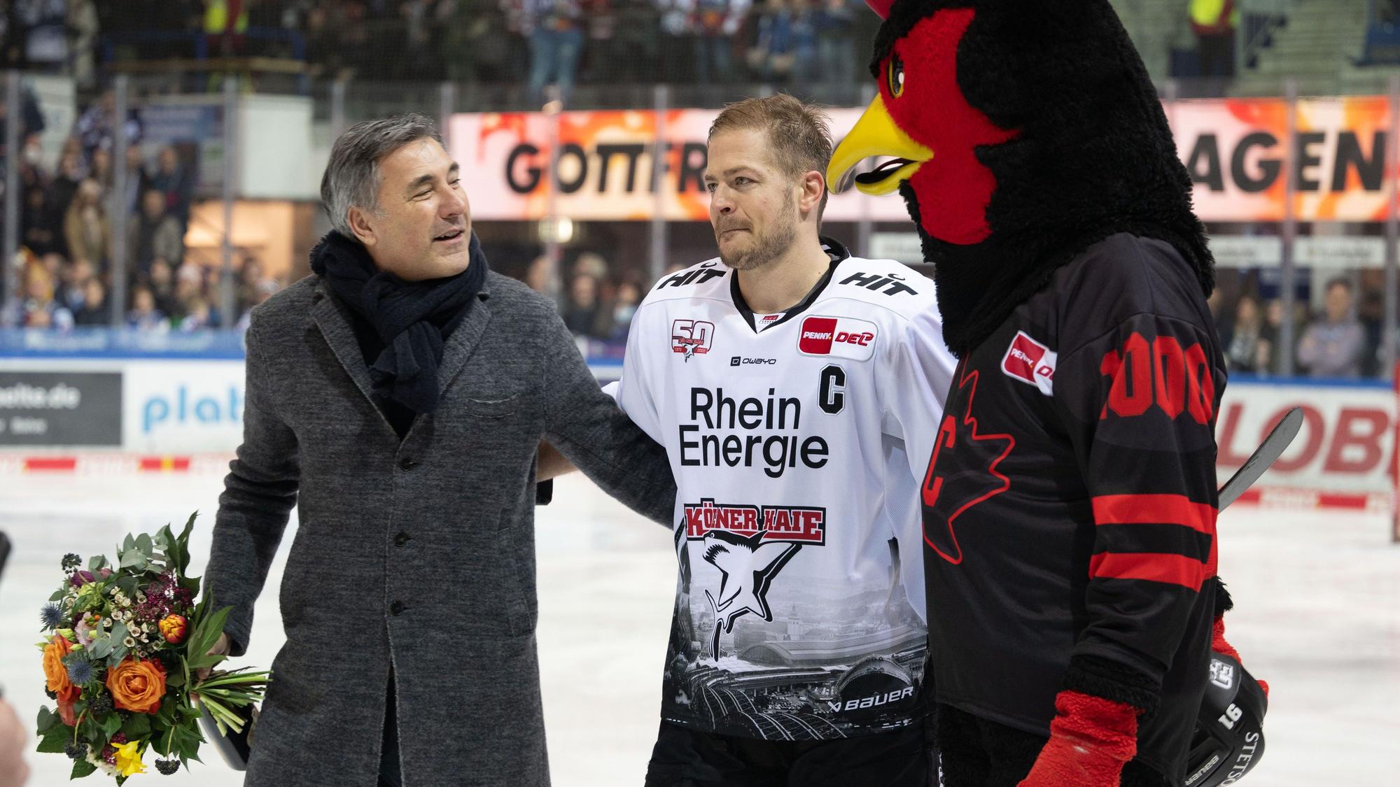 24.02.2023, Nordrhein-Westfalen, Iserlohn: Eishockey: DEL, Iserlohn Roosters - Kölner Haie, Hauptrunde, 46. Spieltag, Eissporthalle Iserlohn: Moritz Müller (M) wird vor dem Spiel für sein 1000. Spiel geehrt. Rechts Maskottchen Icey von den Rooster. Links Wolfgang Brück, Geschäftsführer der Iserlohn Roosters. Foto: Bernd Thissen/dpa +++ dpa-Bildfunk +++