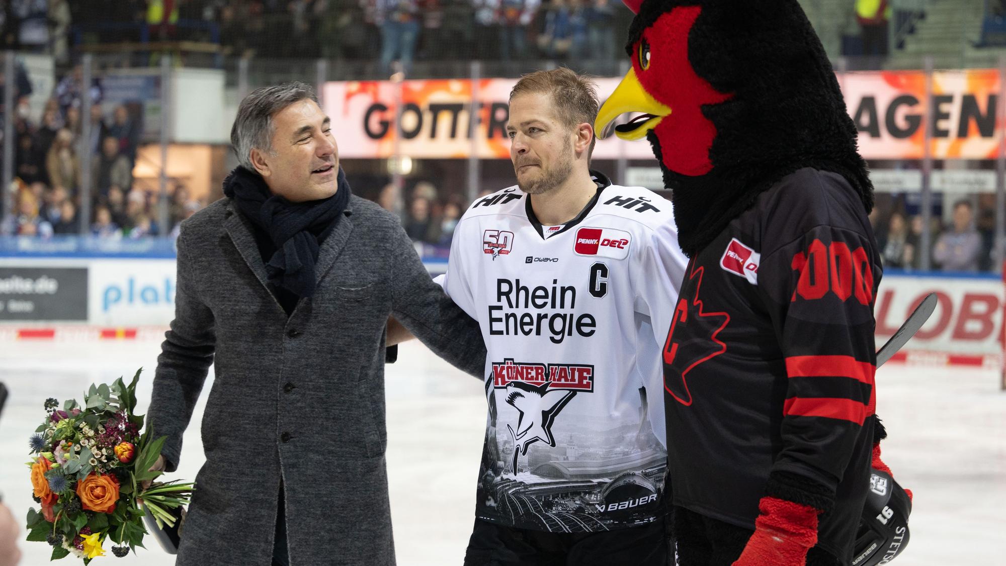 24.02.2023, Nordrhein-Westfalen, Iserlohn: Eishockey: DEL, Iserlohn Roosters - Kölner Haie, Hauptrunde, 46. Spieltag, Eissporthalle Iserlohn: Moritz Müller (M) wird vor dem Spiel für sein 1000. Spiel geehrt. Rechts Maskottchen Icey von den Rooster. Links Wolfgang Brück, Geschäftsführer der Iserlohn Roosters. Foto: Bernd Thissen/dpa +++ dpa-Bildfunk +++