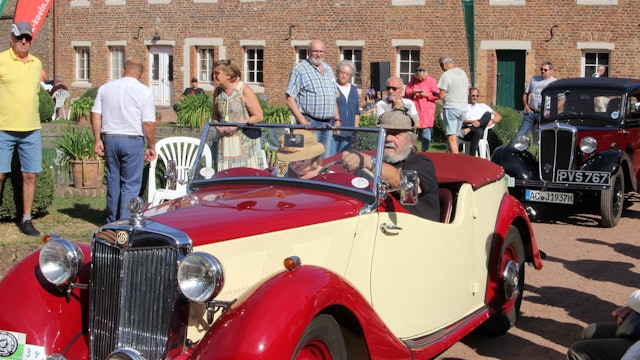 Zwei alte Autos stehen hintereinander auf einem Weg. Neben dem Weg stehen mehrere Zuschauer.