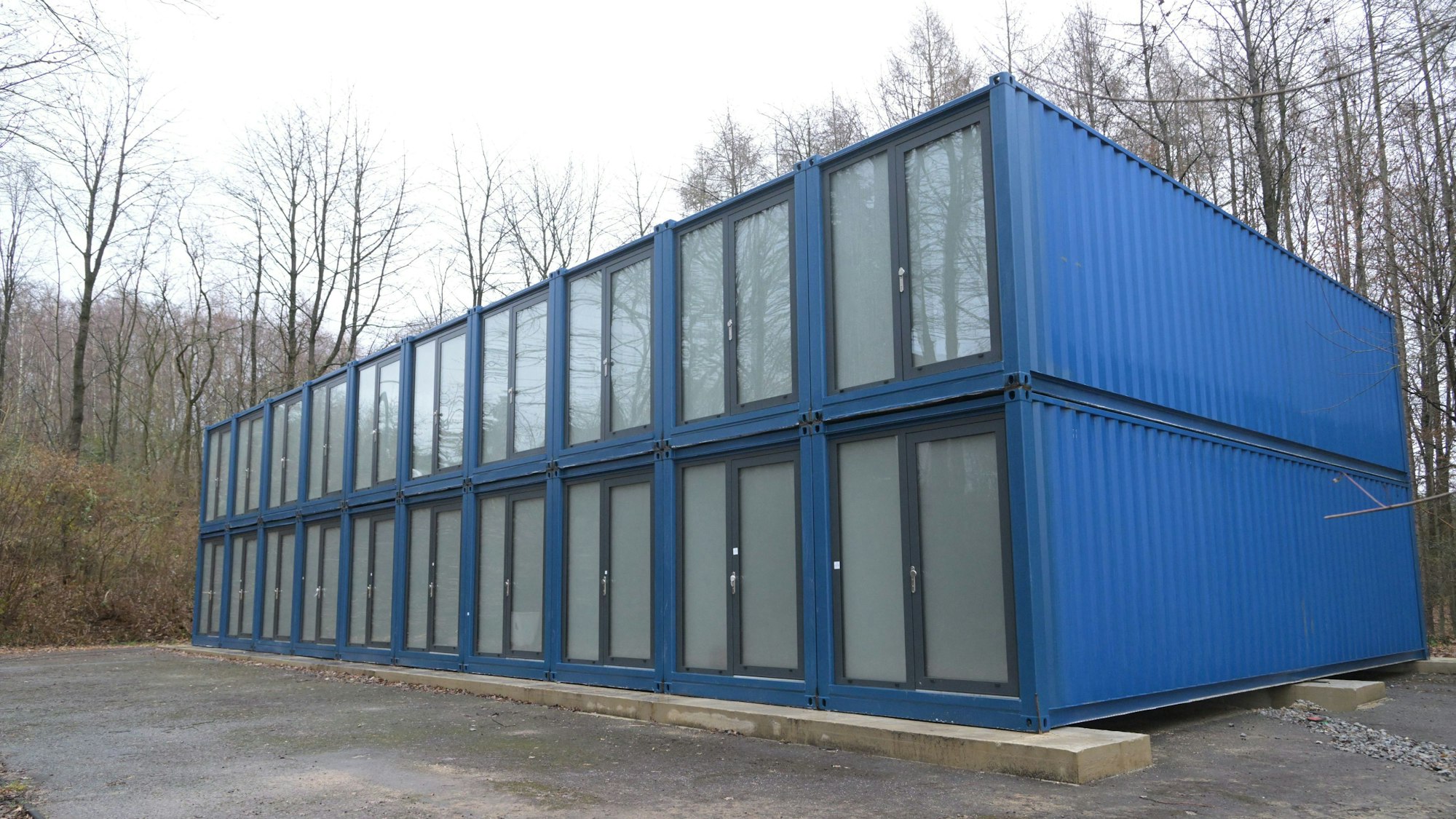 Blaue Unterkunft/Container für Geflüchtete Flüchtlinge in Odenthal stehen auf einem Parkplatz am Wald.