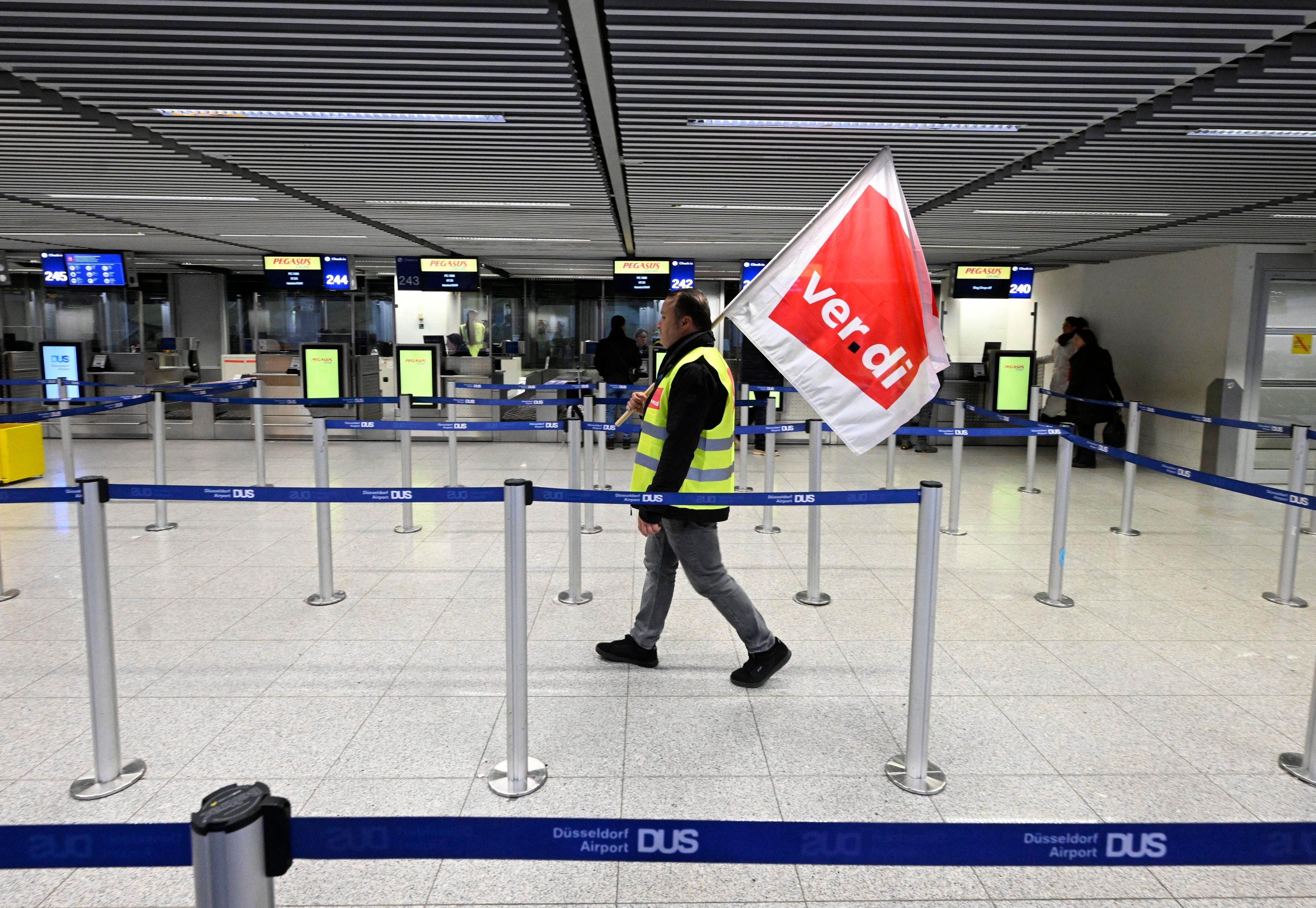 Es ist ein Mann zu sehen, der mit einer Verdi-Flagge durch den leeren Flughafen läuft.