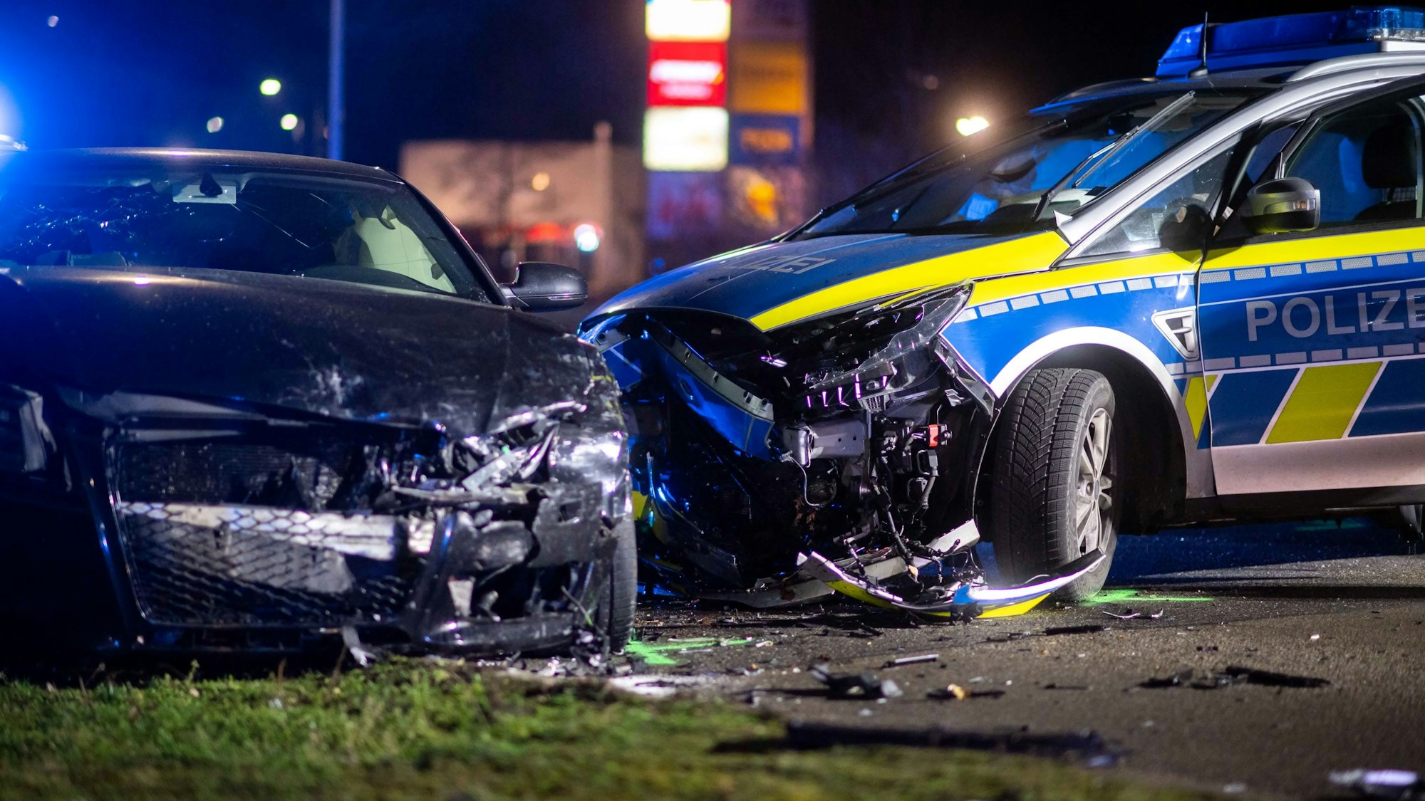 Ein schwarzer Audi und ein Polizeiauto stehen stark demoliert auf der Straße.