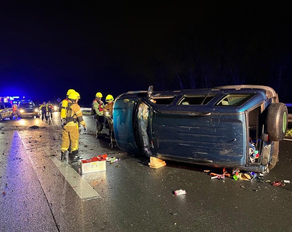 Feuerwehrleute stehen an dem verunglücktem Auto. Auf der Fahrbahn liegen Trümmerteile.