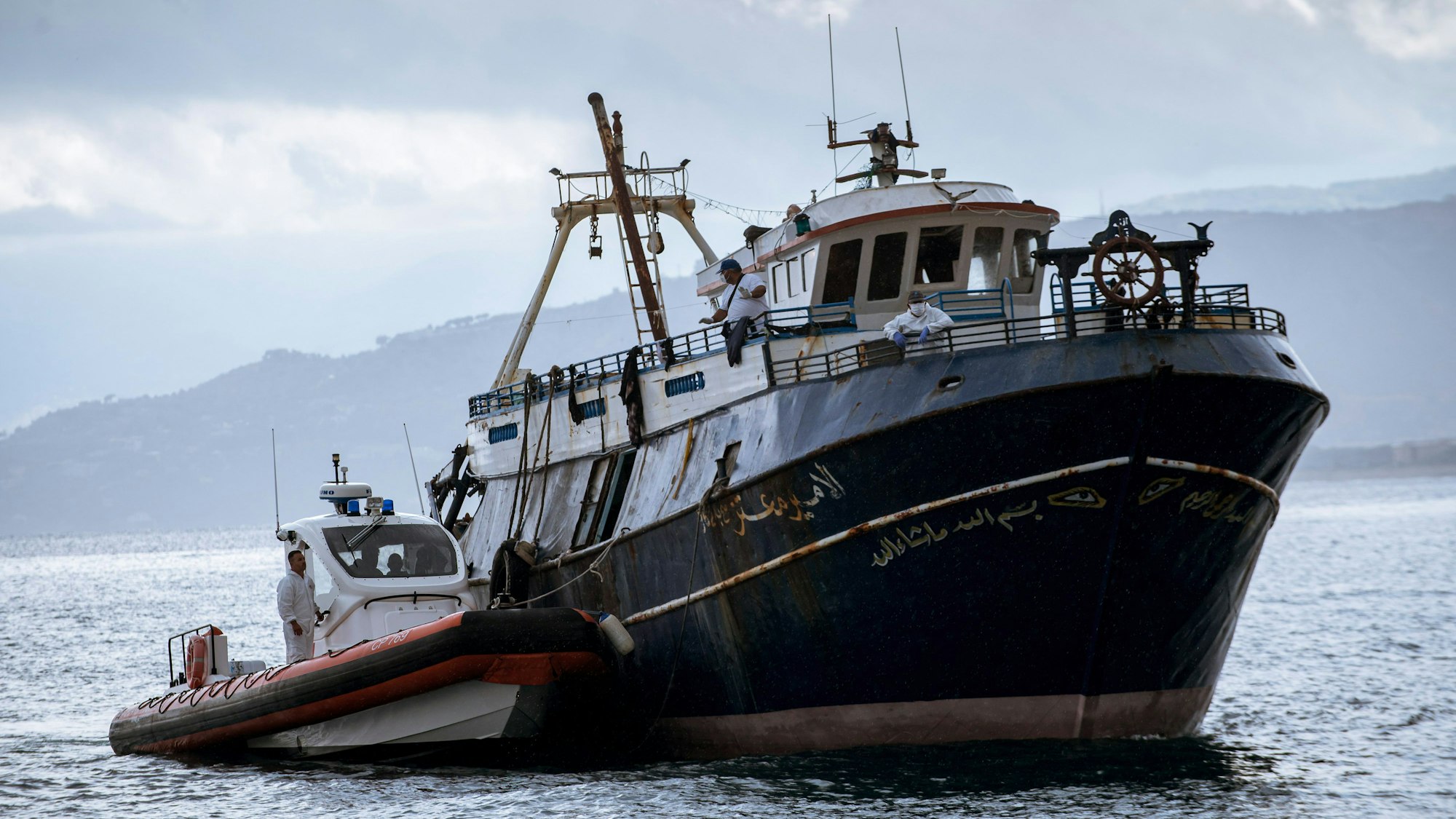 Patrouillenboot fährt mit dem Boot der Migranten in den Hafen ein.