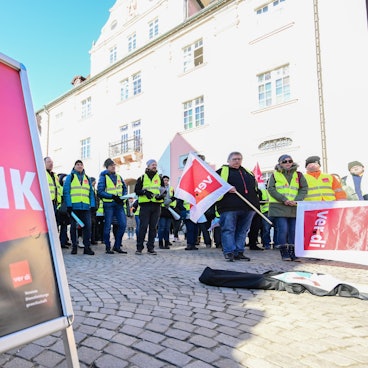 Mitglieder der Gewerkschaft Verdi stehen bei einer Kundgebung mit Fahnen auf einem Marktplatz in Rottenburg, Baden-Württemberg.