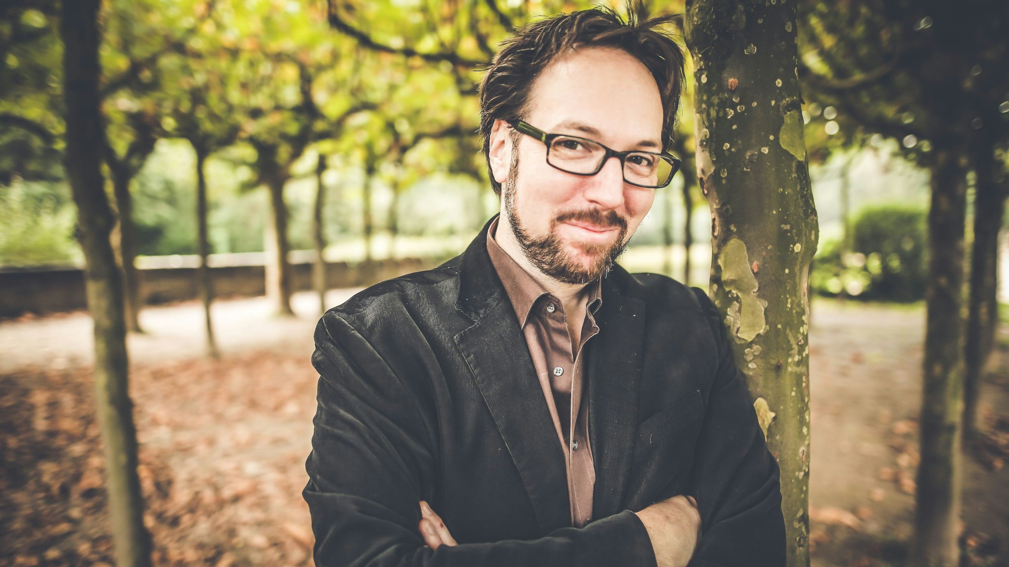 Ein Mann mit Bart und Brille in einer Parkanlage.