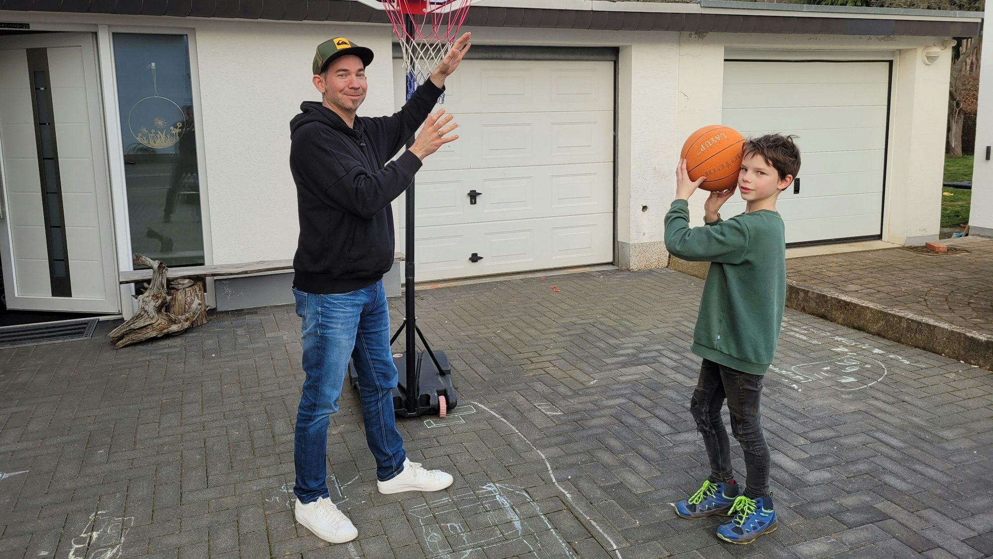 Nick Mertens steht mit seinem Vater in der Einfahrt und spielt Basketball.