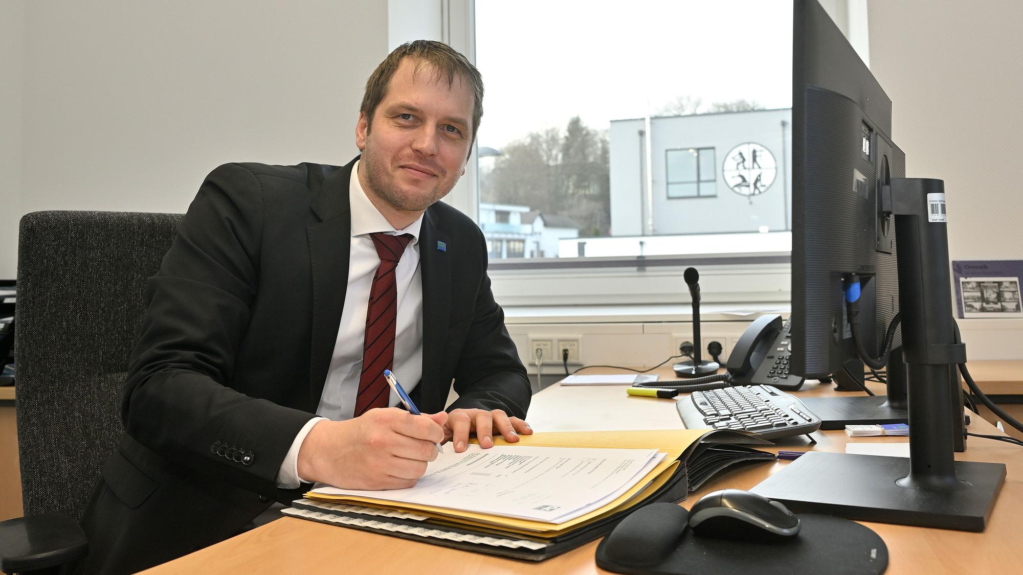 Marc Bredow sitzt am Schreibtisch und lächelt in die Kamera