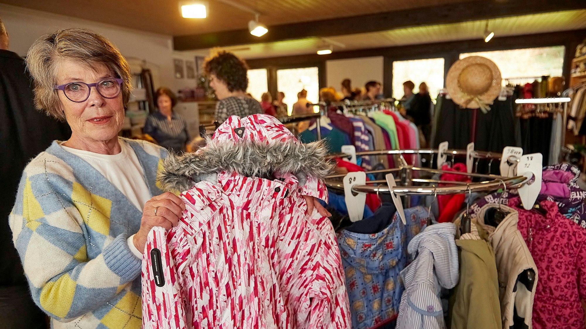 Leiterin Inge Wergen hält ein Kleidungsstück in der Hand. Im Hintergrund sieht man die Räumlichkeiten der neuen Kleiderkammer.