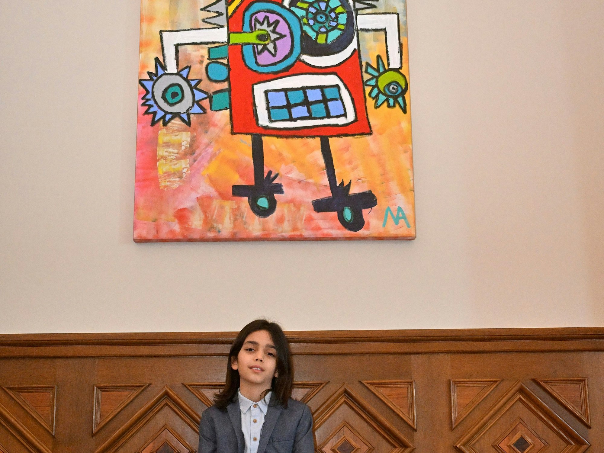 Mikail Akar lehnt an einer holzvertäfelten Wand. Über ihm hängt eins seiner Werke.