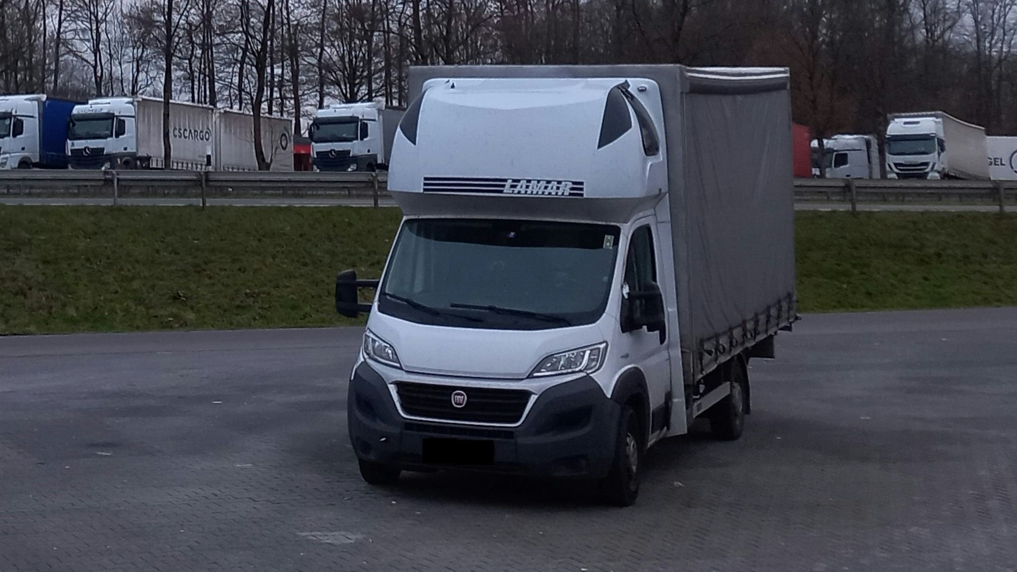 Zu sehen ist ein Autobahnparkplatz mit einem kleinen Transporter im Vordergrund, der auf einem für ihn viel zu großen Parkplatz abgestellt wurde.