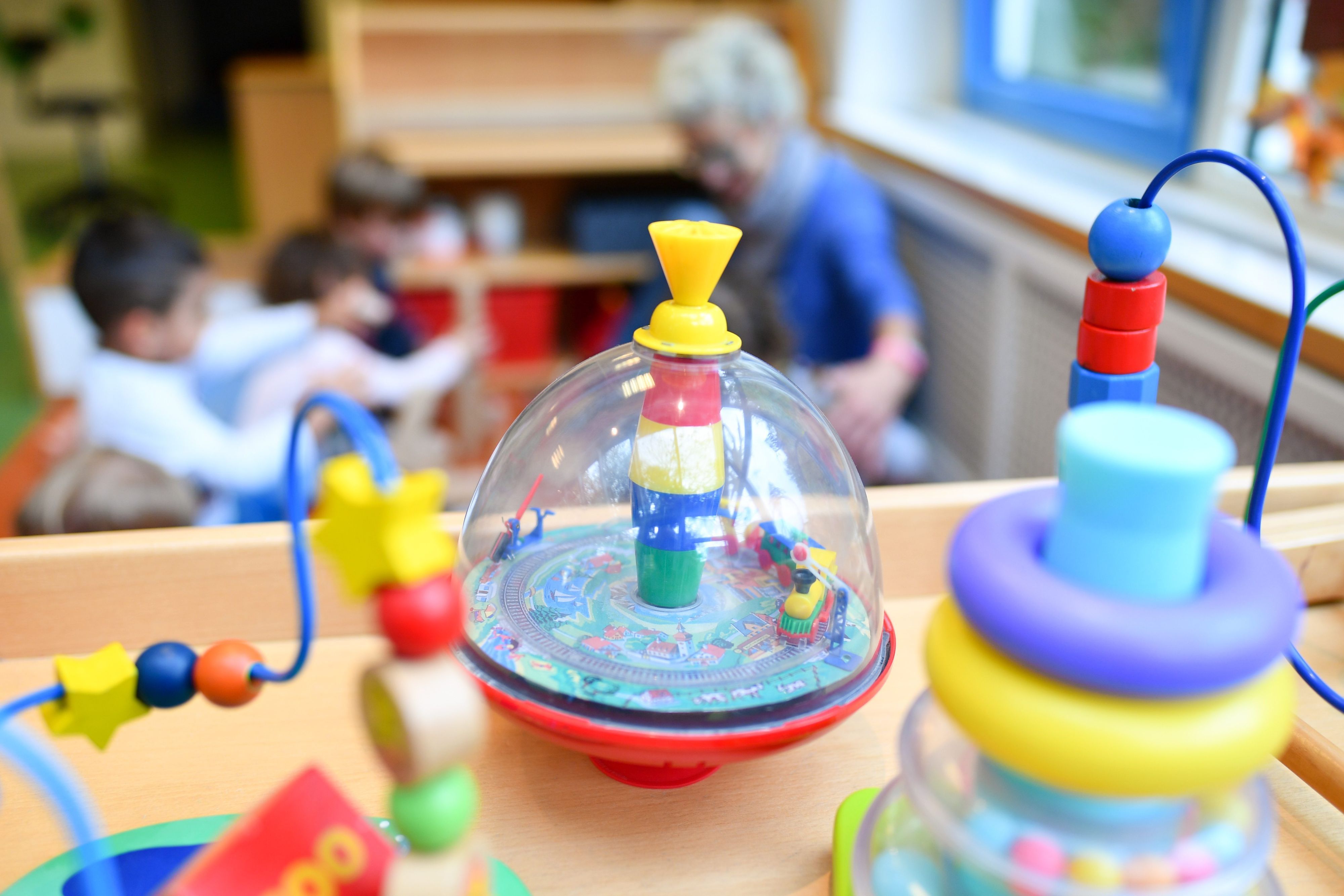 Eine Erzieherin spielt in einer Kita mit Kindern. Im Vordergrund steht Spielzeug.