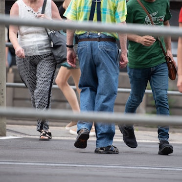 Es sind die Unterkörper mehrere Menschen zu sehen, die über die Straße laufen. Der Fokus des Bildes liegt auf dem Fußverkehr im Straßenverkehr.