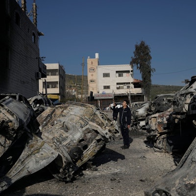 Ausgebrannte und verkohlte Autos liegen auf den Straßen der Stadt Huwara. Ein Mann läuft zwischen den Autos umher.