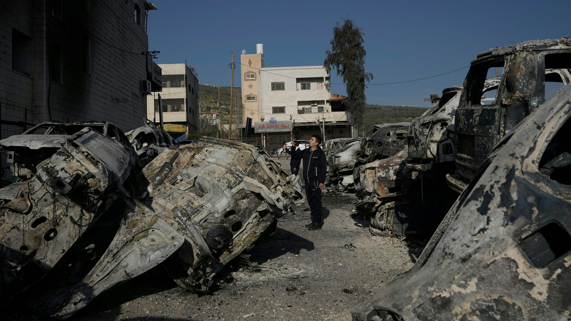 Ausgebrannte und verkohlte Autos liegen auf den Straßen der Stadt Huwara. Ein Mann läuft zwischen den Autos umher.