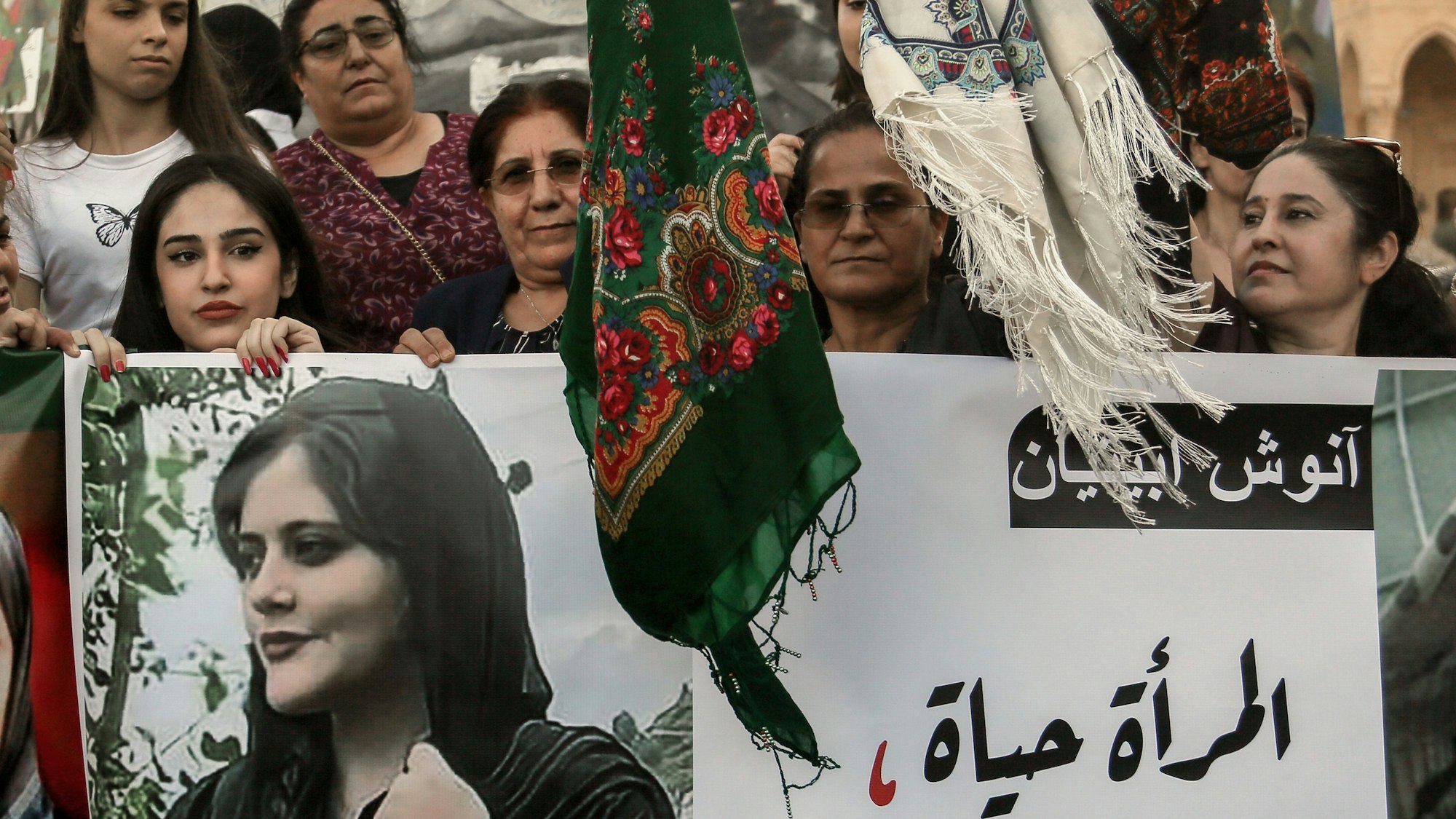 Kurdische Frauen schwenken bei einer Demonstration Kopftücher, während sie Bilder von Mahasa Amini in die Höhe halten.