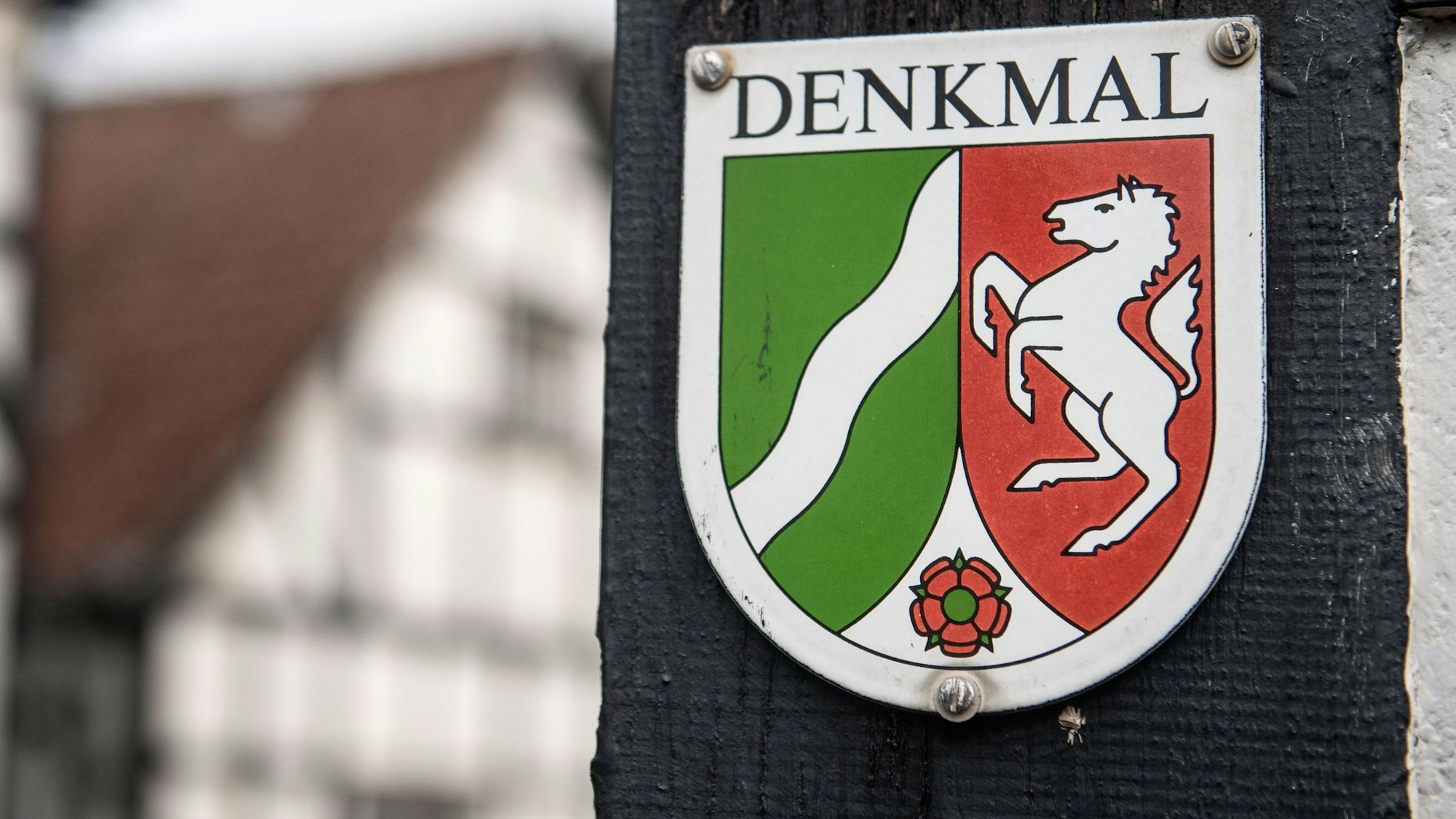 Ein Nordrhein-Westfälisches Denkmal-Schild mit der Aufschrift «Denkmal» ist am Balken eines Fachwerkhauses befestigt.