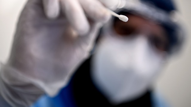 Ein Arzt hält ein Teststäbchen für die Entnahme einer Probe für einen PCR-Test in der Hand.