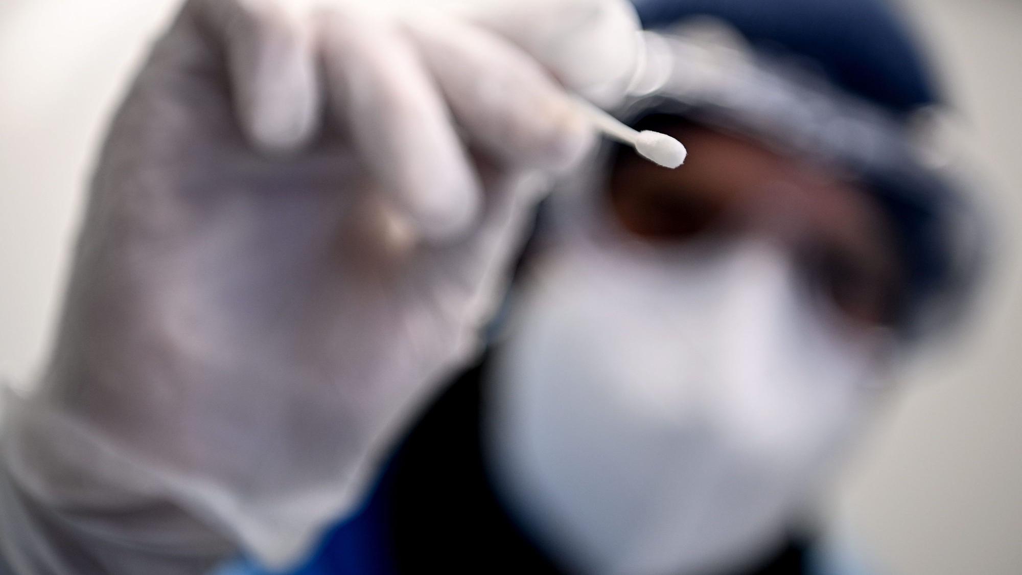 Ein Arzt hält ein Teststäbchen für die Entnahme einer Probe für einen PCR-Test in der Hand.