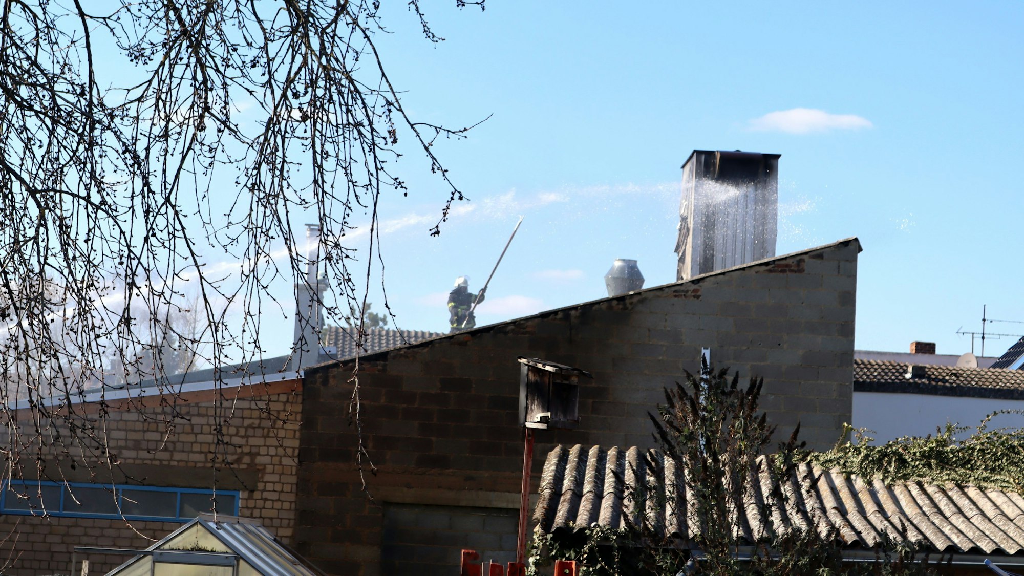 Ein Feuerwehrmann öffnet mit einem Haken das Dach des Betriebes.