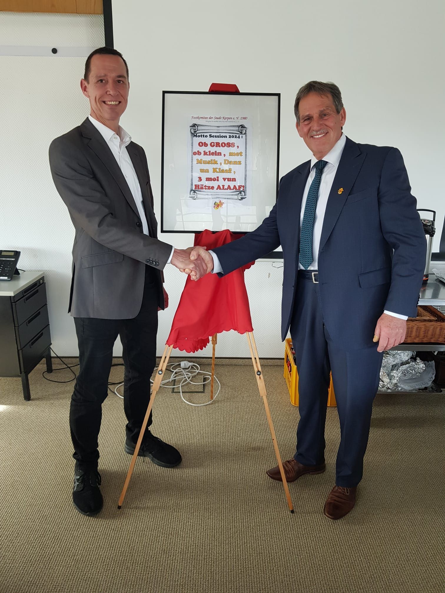 Das Foto zeigt Kerpens Bürgermeister Dieter Spürck und den Karnevalisten Jürgen Mein mit dem neuen Sessionsmotto.