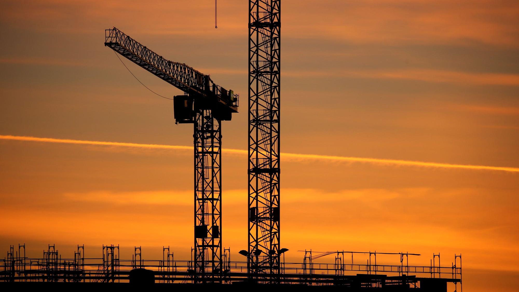 Baukräne einer Großbaustelle stehen im Sonnenaufgang.