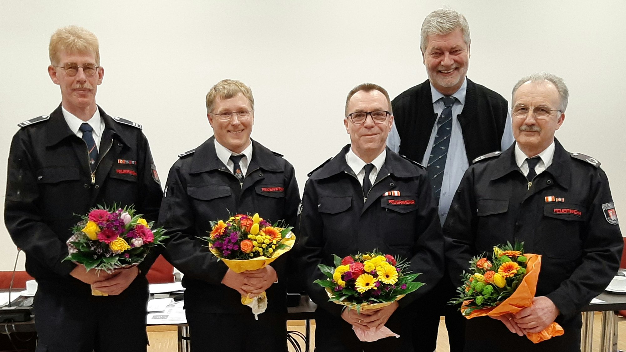 Neue und alte Wehrführung mit Blumensträußen und Bürgermeister Hilko Redenius im Ratssaal.