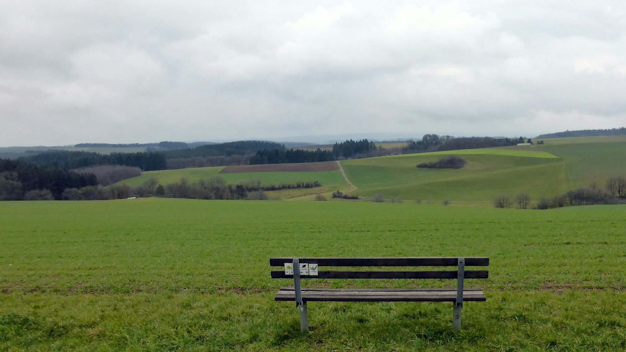 Eine Bank steht vor einem weiten Ausblick ins Tal