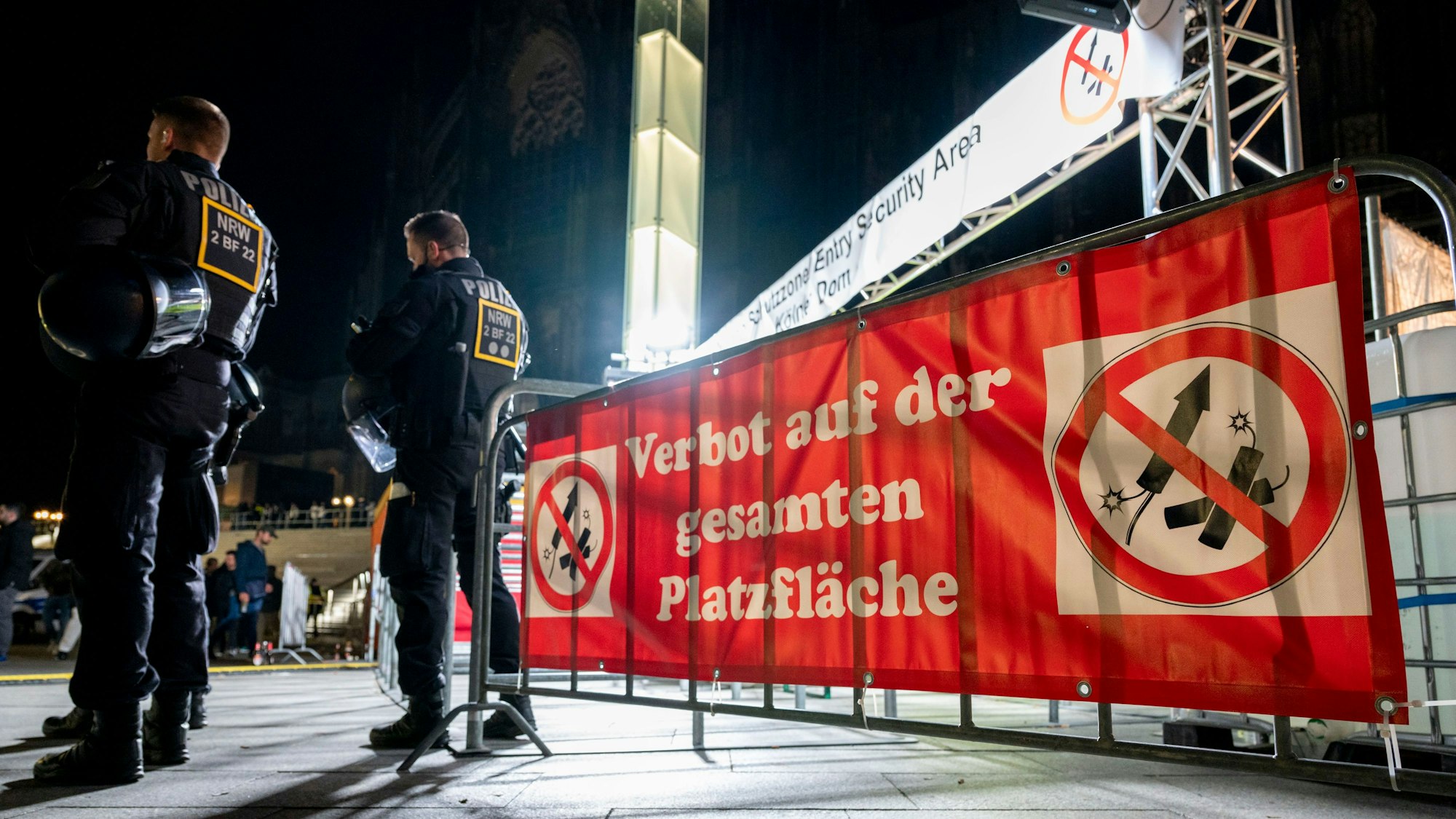 Polizisten stehen an Silvester vor einem Schild, das auf eine Böllerverbotszone hinweist.