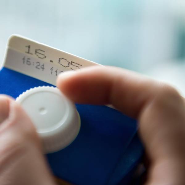 Eine Hand öffnet eine Tüte Milch, auf der eine Mindesthaltbarkeitsdatum steht