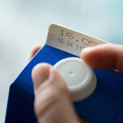 Eine Hand öffnet eine Tüte Milch, auf der eine Mindesthaltbarkeitsdatum steht