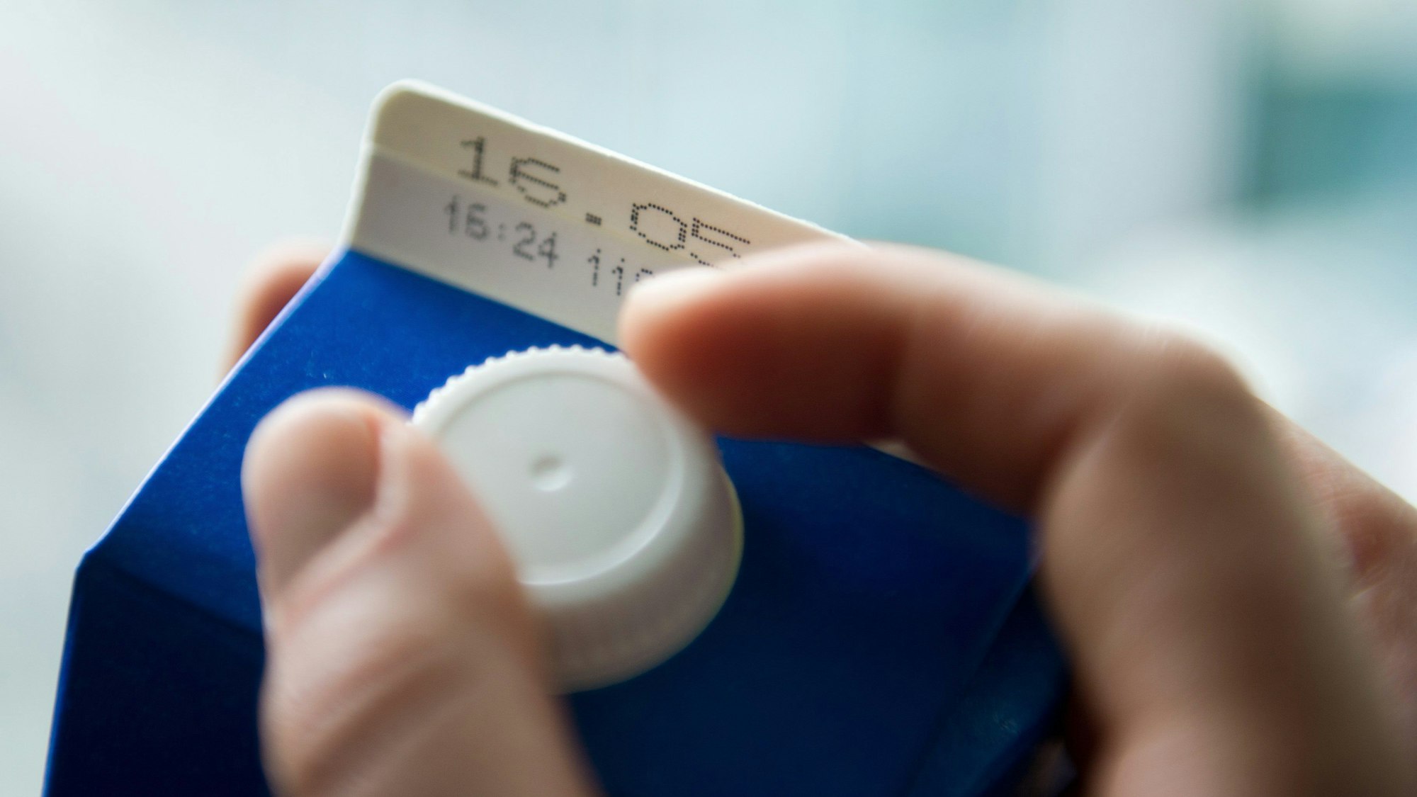 Eine Hand öffnet eine Tüte Milch, auf der eine Mindesthaltbarkeitsdatum steht