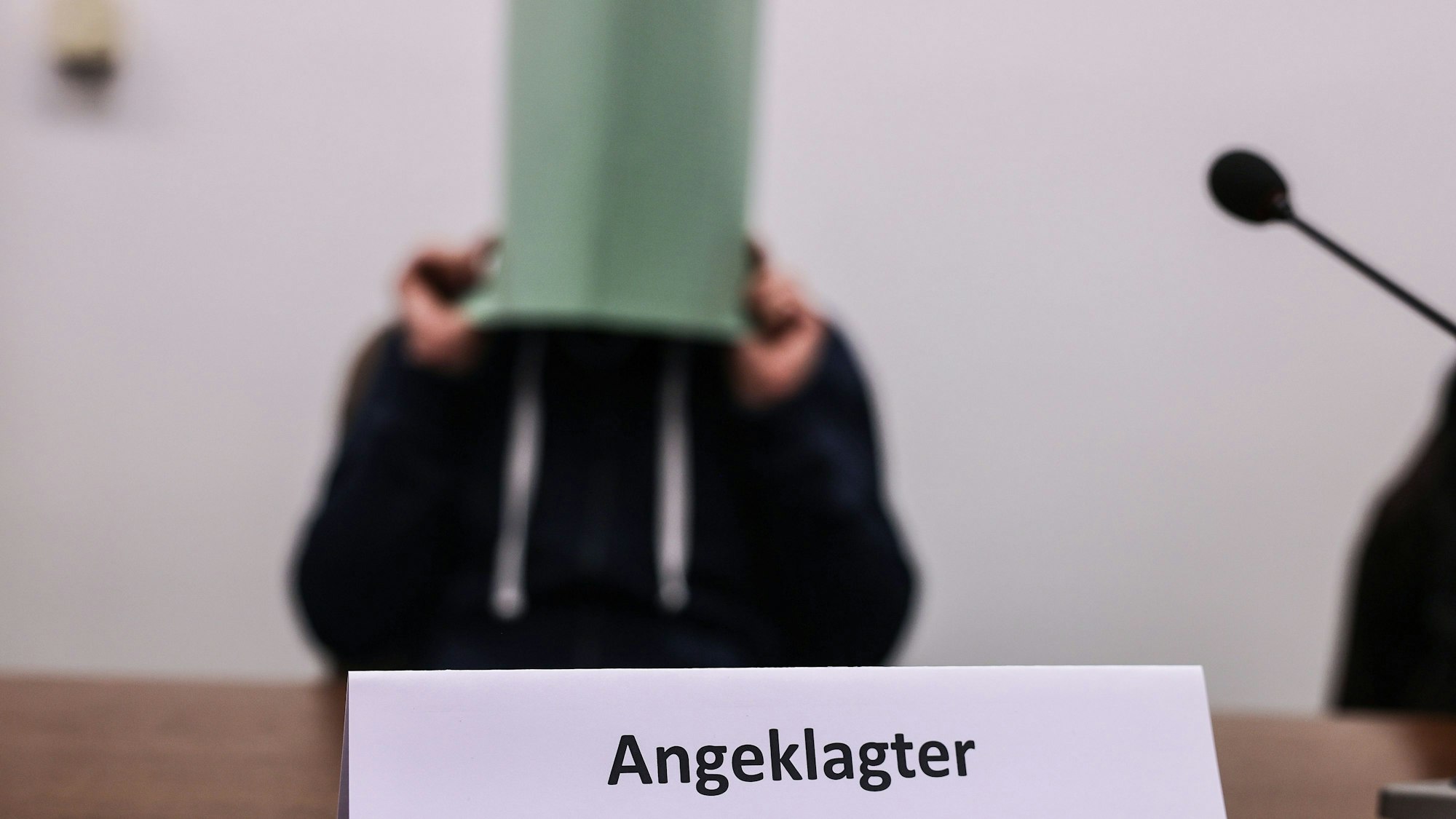Der Angeklagte im Missbrauchskomplex Wermelskirchen hält sich im Gerichtssaal eine Mappe vor das Gesicht. Der Mann soll sich im Internet als Babysitter angeboten und so Kontakt zu den Familien der Opfer bekommen haben.