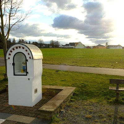 Hinter einem Heiligenhäuschen liegt ein Acker.