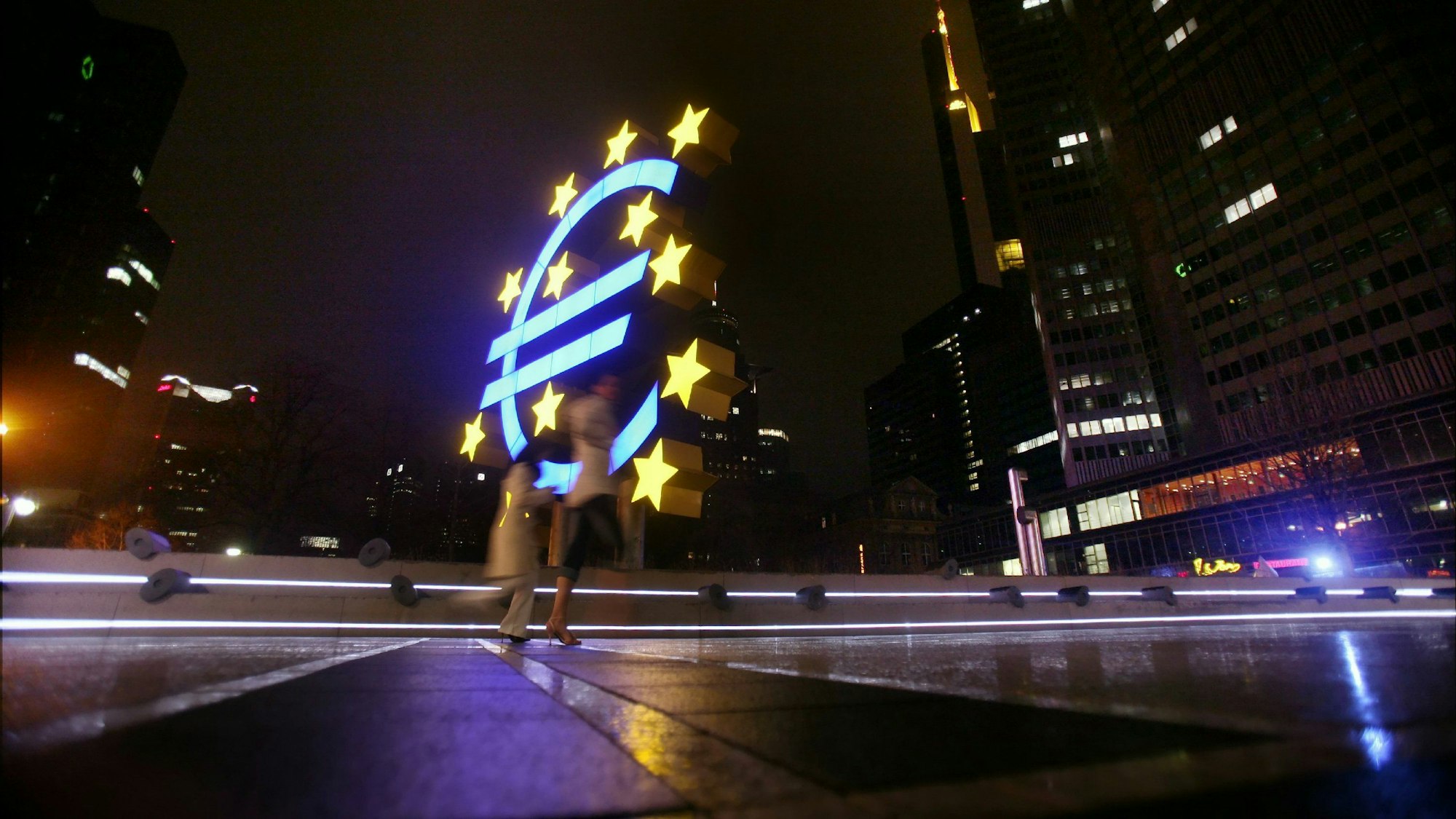 Passanten gehen an der beleuchteten Skulptur, die ein von Sternen umgebenes Euro-Symbol zeigt, vor dem Gebäude der Europäischen Zentralbank (EZB) in Frankfurt am Main vorbei.